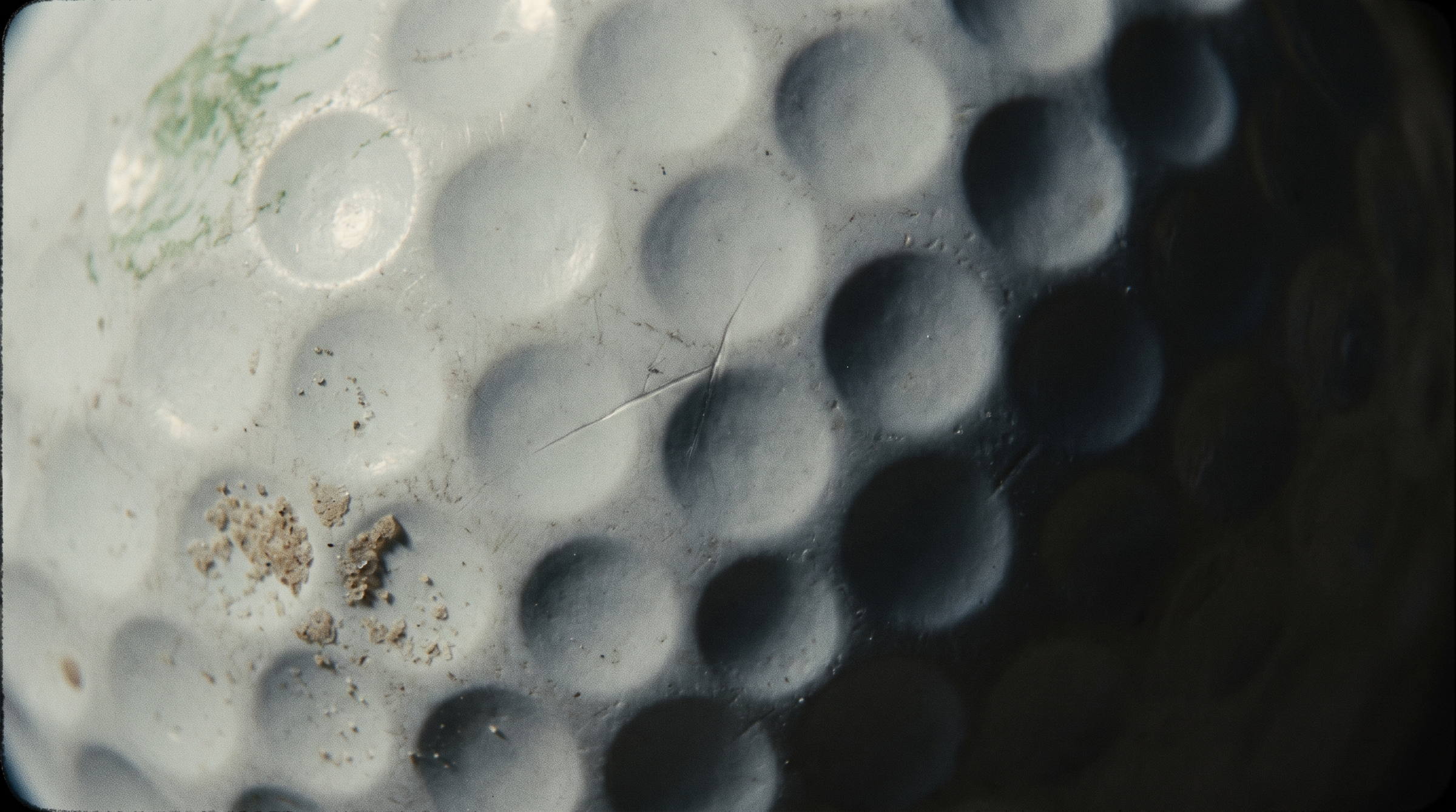 Extreme macro of a scuffed golf ball, dimples raking in low light.