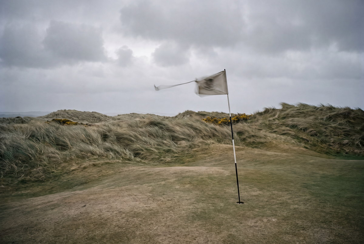 A flagstick bent sideways in strong coastal wind.